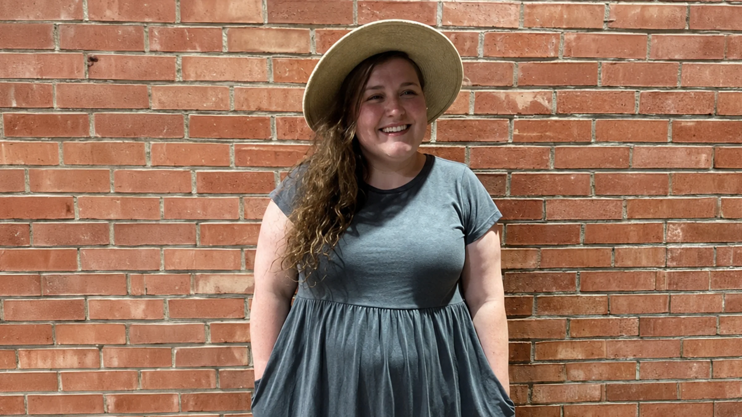 Kaitlynn King smiling in a sunhat in front of a brick wall